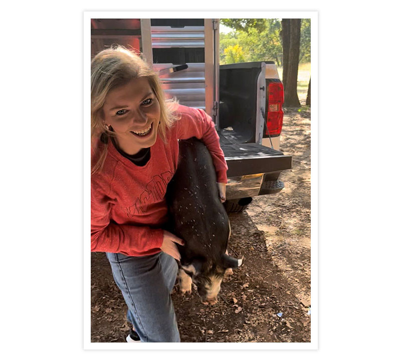 A woman wearing a red long-sleeve shirt holding a baby pig while getting it out of the truck.